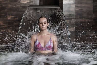 Sakin genç, sıska bir kadın lüks spa merkezinde vakit geçirirken kristal fışkırtan su jetiyle havuzda hidroterapi masajının keyfini çıkarıyor.