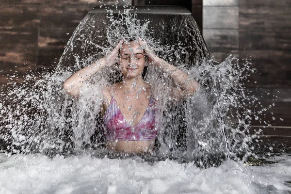 Позитивная Молодая Женщина Наслаждается Процедурой Гидротерапии Брызгает Водой Стоя Струей — стоковое фото
