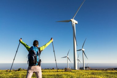 Tanımlanamayan erkek kaşifin geri planda durup kaldırılmış ellerde yürüyüş direkleri ile Lanzarote 'deki yel değirmenlerinin arka planında elde edilen başarıyı kutlaması.
