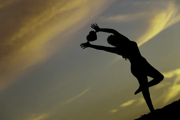 Bir kalp arkadan aydınlatmalı günbatımında tutan genç kadın