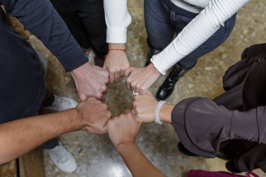 Ortak çalışma alanındaki bir grup birey birlik ve işbirliği gösterisi için yumruklaşıyor. Bu an, beyin fırtınası yapan profesyoneller arasındaki takım çalışmasının ruhunu yansıtıyor..