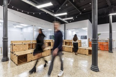 Ortak bir çalışma alanında, bireyler işle ilgili faaliyetlerde bulunurlar. Odada ahşap mobilyalar ve üretkenlik için tasarlanmış parlak bir atmosfer bulunuyor..