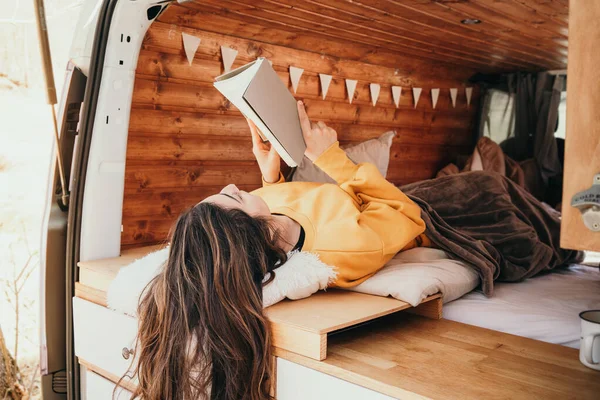 Vanlife - Młoda kobieta leżąca w specjalnie skonwertowanym vanie czytając książkę — Zdjęcie stockowe