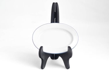 Siyah plastik ekranda mavi kenarlı beyaz oval seramik plaka beyaz arka planda izole edilmiş.