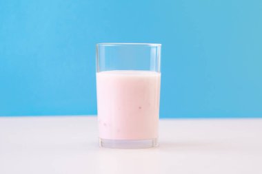 Mavi arka planda bir bardakta taze çilekli yoğurt.