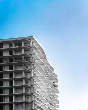 Mavi gökyüzüne karşı dalgalı cephe mimarisi olan modern beton bina yapım aşamasında.