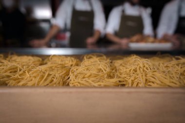 Şefin arka planında odağını kaybetmiş birkaç porsiyon makarna.