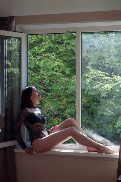 窓の上に座っている黒いボディライナーの女性 — ストック写真