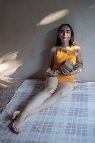 Woman in the ochre underwear sitting on the sofa and holding the flowers immortelles