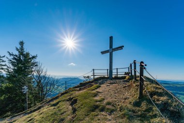 Uçsuz bucaksız dağlar ve berrak mavi gökyüzü haçı bir tepenin üzerine yerleştirir. Bu da Oberstaufen yakınlarındaki Nagelfluhkette 'de doğa güzelliği ile yapılan ruhani bir yolculuğun göstergesidir.