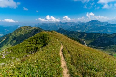 Huzurlu bir yürüyüş yolu, berrak gökyüzünün altındaki görkemli tepelerin panoramik manzarasını sunan, dinginliği ve hayranlık uyandıran doğal güzelliği uyandıran canlı dağların arasından esiyor.