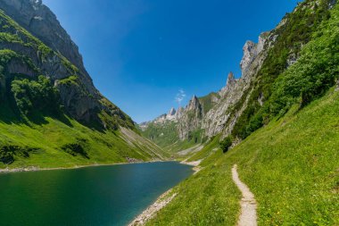 Saemtisersee ve Faehlensee göllerini aşan sakin bir dağ yolu engebeli tepeler ve yemyeşil çimlerle çevrili Appenzell yakınlarındaki Alpstein Dağları 'ndaki parlak gökyüzünün altında.