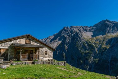 Kırsal taştan bir dağ evi, berrak mavi gökyüzünün altında yükselen tepelere karşı huzur içinde yuva yapar. Huzur ve alp ihtişamı uyandırır.