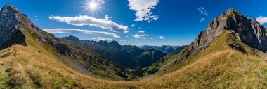 Nefes kesici bir panoramik manzara Alplerin ihtişamını yakalar, sakin vadileri ve parlak güneş ışığı altında engebeli tepeleri gösterir, barış ve macera çağrıştırır.