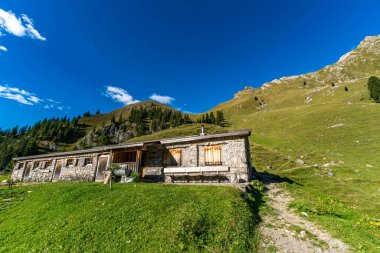Sakin bir dağ evi otlak bir yamaçta huzur içinde duruyor, berrak gökyüzü ve altın güneş ışığı altında huzur ve macera çağrıştırıyor.