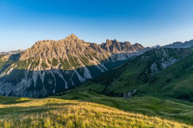 Altın güneş ışığı, Tannheimer Vadisi 'nde engebeli alp tepeleri ve yemyeşil çayırlar, nefes kesen bir göl yürüyüşü sırasında huzur ve korkuyu çağrıştırıyor.
