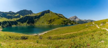 Zümrüt yamaçların arasına kurulmuş sakin bir alp gölünün nefes kesici panoramik görüntüsü barış ve macerayı çağrıştırıyor.