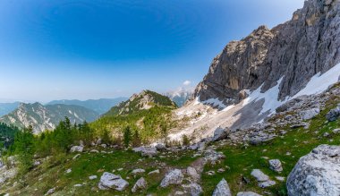 Nefes kesici bir dağ manzarası Mala Mojstrovka 'nın engebeli güzelliğini yakalar, kar kaplı zirveler berrak gökyüzü altında canlı yeşil çayırlar ile tezat oluşturur, dinginlik ve macera çağrıştırır.