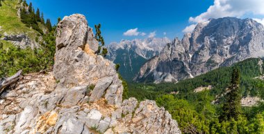 Sivri tepelerin ve yemyeşil vadilerin nefes kesici manzarası, Triglav Ulusal Parkları 'ndaki güneşli dağ yürüyüşü sırasında korku ve sükuneti çağrıştırıyor.