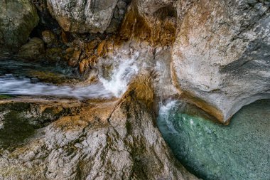 Güçlü bir şelale, Martuljek Vadisi 'ndeki engebeli, mineral zengini kayalara doğru zarif bir şekilde dalıyor. Huzur ve ham doğal güzelliği gün ışığı altında uyandırıyor.