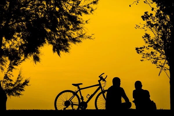 Zwei Personen sitzen bei Sonnenuntergang mit einem Fahrrad. — Stockfoto