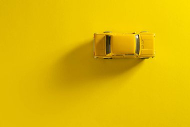 Sarı arka planda uzun ve yan gölgeli sarı bir oyuncak arabanın üst görüntüsü.