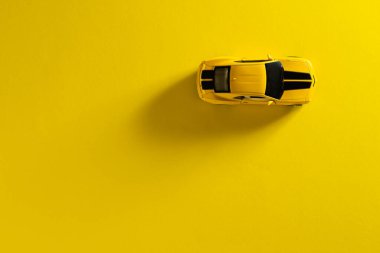 İzmir, Türkiye - 30 Eylül 2020: Sarı arka planda uzun ve yan gölgeli sarı bir oyuncak arabanın üst görünümü.