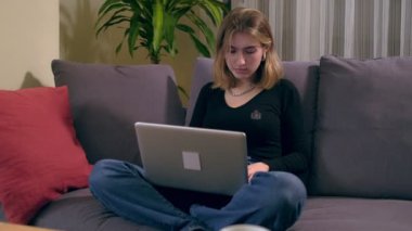 Genç Türk kadın kanepede otururken dizüstü bilgisayar kullanıyor.  
