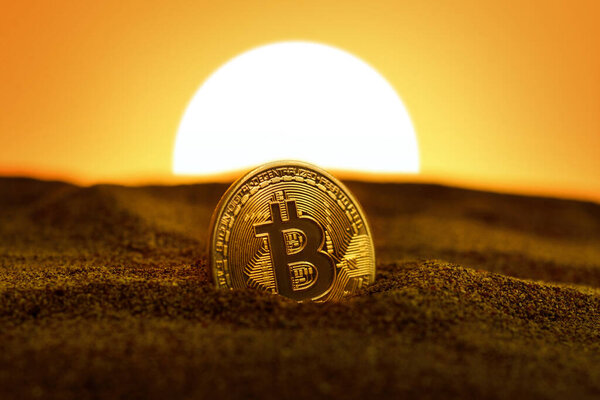 Крупный план биткойна на песке и на закате.