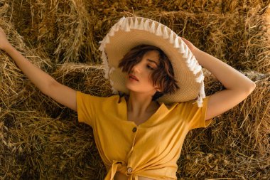 Samanlıkta oturan, sarı gömlekli, hasır şapkalı bir kadının portresi..