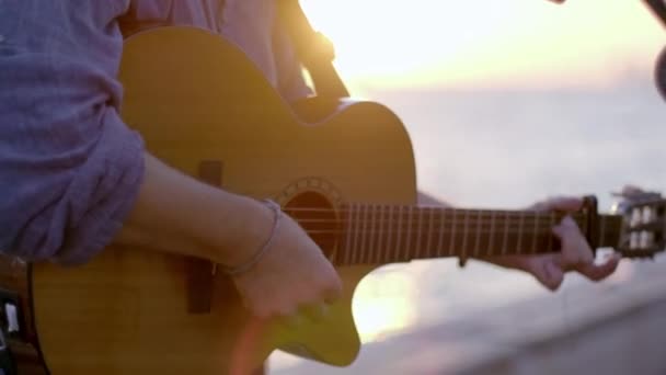 日没と水辺でクラシックギターを演奏するギタリストのショットを閉じます — ストック動画