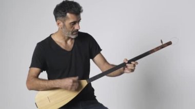 Kopuz çalan Ortadoğulu adam, beyaz arka planda üç telli Baglama adında bir telli çalgıdır..