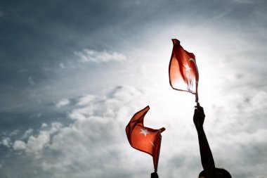 Mavi ve bulutlu gökyüzünde ve özgürlük gününde Türk bayraklarını tutan İki El İzmir.