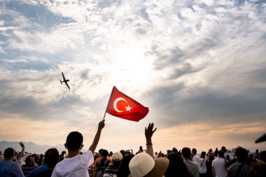 İzmir, Türkiye - 9 Eylül 2021: Bir gösteri için İzmir 'in özgürlük gününde gökyüzünde uçan bir uçak. Çerçevede Türk bayrağı sallayan insanlar