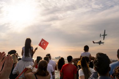 İzmir, Türkiye - 9 Eylül 2021: İzmir 'in özgürlük gününde bir gösteri için gökyüzünde uçan uçaklar. Çerçevede Türk bayrağı sallayan insanlar