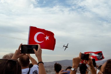 İzmir, Türkiye - 9 Eylül 2021: Bir gösteri için İzmir 'in özgürlük gününde gökyüzünde uçan bir uçak. Çerçevede Türk bayrağı sallayan insanlar