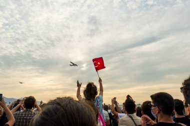 İzmir, Türkiye - 9 Eylül 2021: Bir gösteri için İzmir 'in özgürlük gününde gökyüzünde uçan bir uçak. Çerçevede Türk bayrağı sallayan bir kız ve kalabalık çan kulesi.