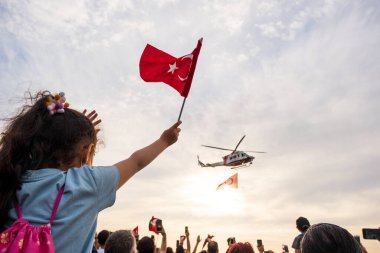 İzmir, Türkiye - 9 Eylül 2021: Bir gösteri için İzmir 'in özgürlük gününde, dev bir Türk bayrağıyla gökyüzünde uçan Türk Sahil Güvenlik helikopteri. Çerçevede Türk bayrağı sallayan bir kız.
