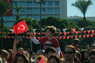 İzmir, Türkiye - 29 Ekim 2025: Alsancak Meydanı 'nda düzenlenen Cumhuriyet Günü kutlamaları sırasında babasının omuzlarında oturan genç çocuk, Türk bayrağını coşkuyla sallıyor