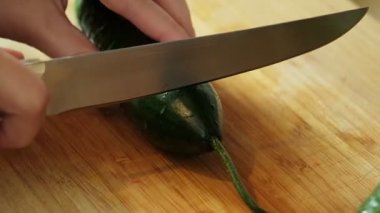 Salata hazırlamak için tahta kesme tahtasındaki bıçakla salatalık dilimleyen bir kadın.