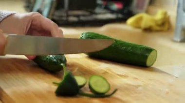 Salata hazırlamak için tahta kesme tahtasındaki bıçakla salatalık dilimleyen bir kadın.