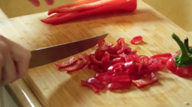 Salata hazırlığı için tahta kesme tahtasının üzerinde kırmızı biber dilimleyen bir kadın.