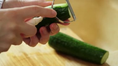 Salata hazırlamak için tahta kesme tahtasının üzerinde sebze soyacağı kullanarak salatalık soyan bir kadın.