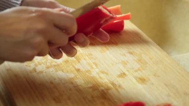 Salata hazırlığı için tahta kesme tahtasının üzerinde kırmızı biber dilimleyen bir kadın.