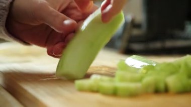 Salata hazırlamak için tahta kesme tahtasındaki bıçakla salatalık dilimleyen bir kadın.