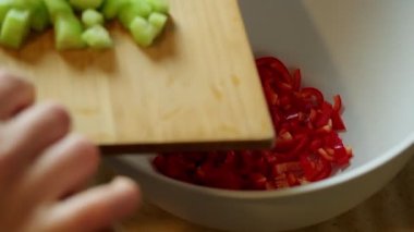 Bir kadın salata yaparken doğranmış salatalıkları tahta kesme tahtasına döküyor.