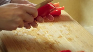 Salata hazırlığı için tahta kesme tahtasının üzerinde kırmızı biber dilimleyen bir kadın.