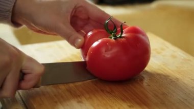 Taze domates doğrayan bir kadın salata hazırlamak için tahta kesme tahtasının üzerinde bıçak kullanıyor.
