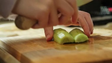 Salata hazırlamak için tahta kesme tahtasındaki bıçakla salatalık dilimleyen bir kadın.
