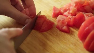 Taze domates doğrayan bir kadın salata hazırlamak için tahta kesme tahtasının üzerinde bıçak kullanıyor.